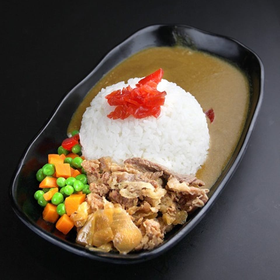 Japanese curry with rice, beef, pickled ginger, peas, and carrots in a black dish.