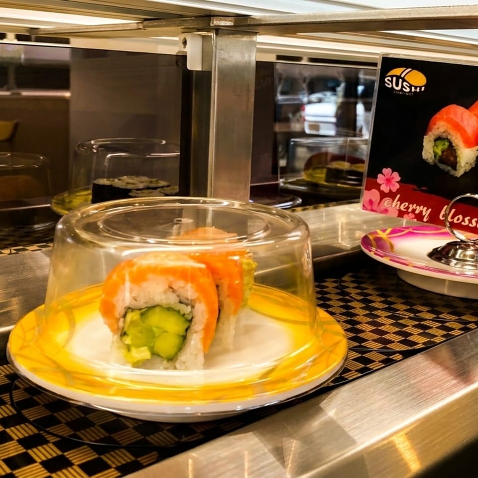 Sushi rolls with salmon and cucumber on a conveyor belt at a sushi restaurant.