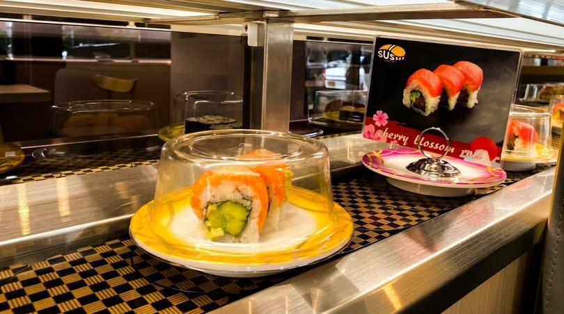 Sushi rolls with salmon and cucumber on a conveyor belt at a sushi restaurant.