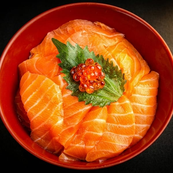 Salmon sashimi slices arranged in a red bowl, garnished with green leaves and bright orange salmon roe.