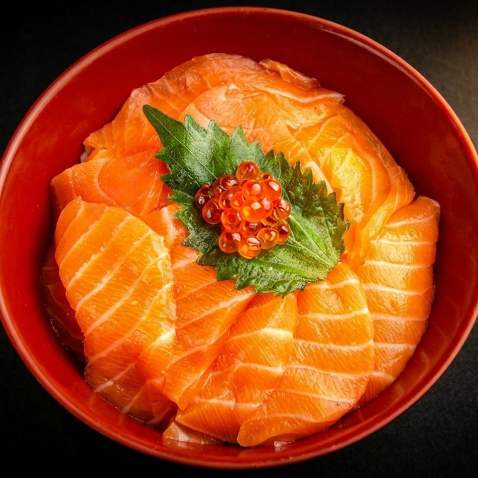 Salmon sashimi slices arranged in a red bowl, topped with green shiso leaf and salmon roe.