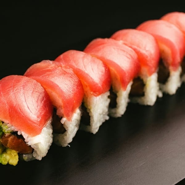 A row of sushi rolls with tuna, avocado, and rice on a dark plate.