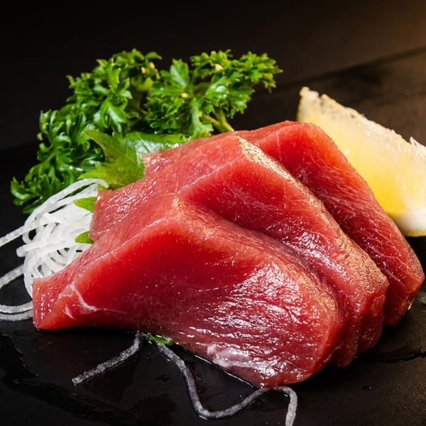 Fresh tuna sashimi slices with shredded daikon, parsley, and a lemon wedge on a dark plate.