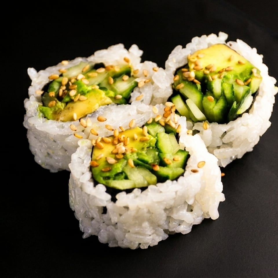 Three sushi rolls with avocado, cucumber, and sesame seeds on a dark surface.