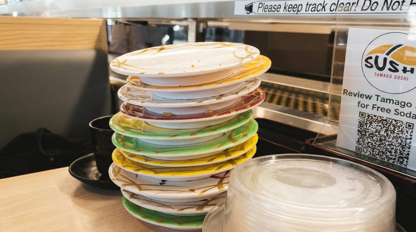 A tall stack of colorful, empty sushi plates on a counter at Tamago Sushi.